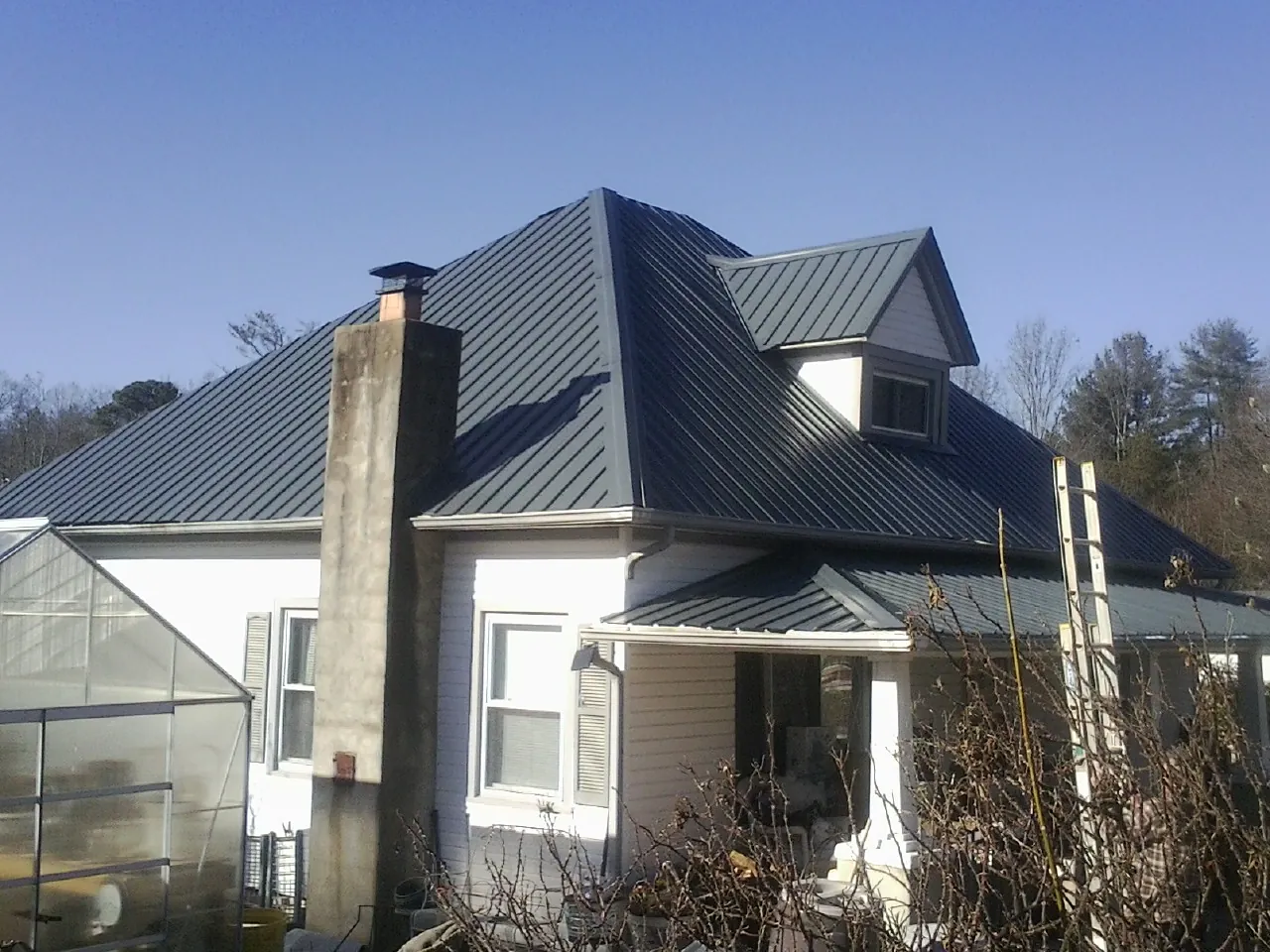 Dark blue standing seam metal roof on a white farmhouse with dormer — Slate & Tile Roof Repair by Roofing Brothers in Caliente