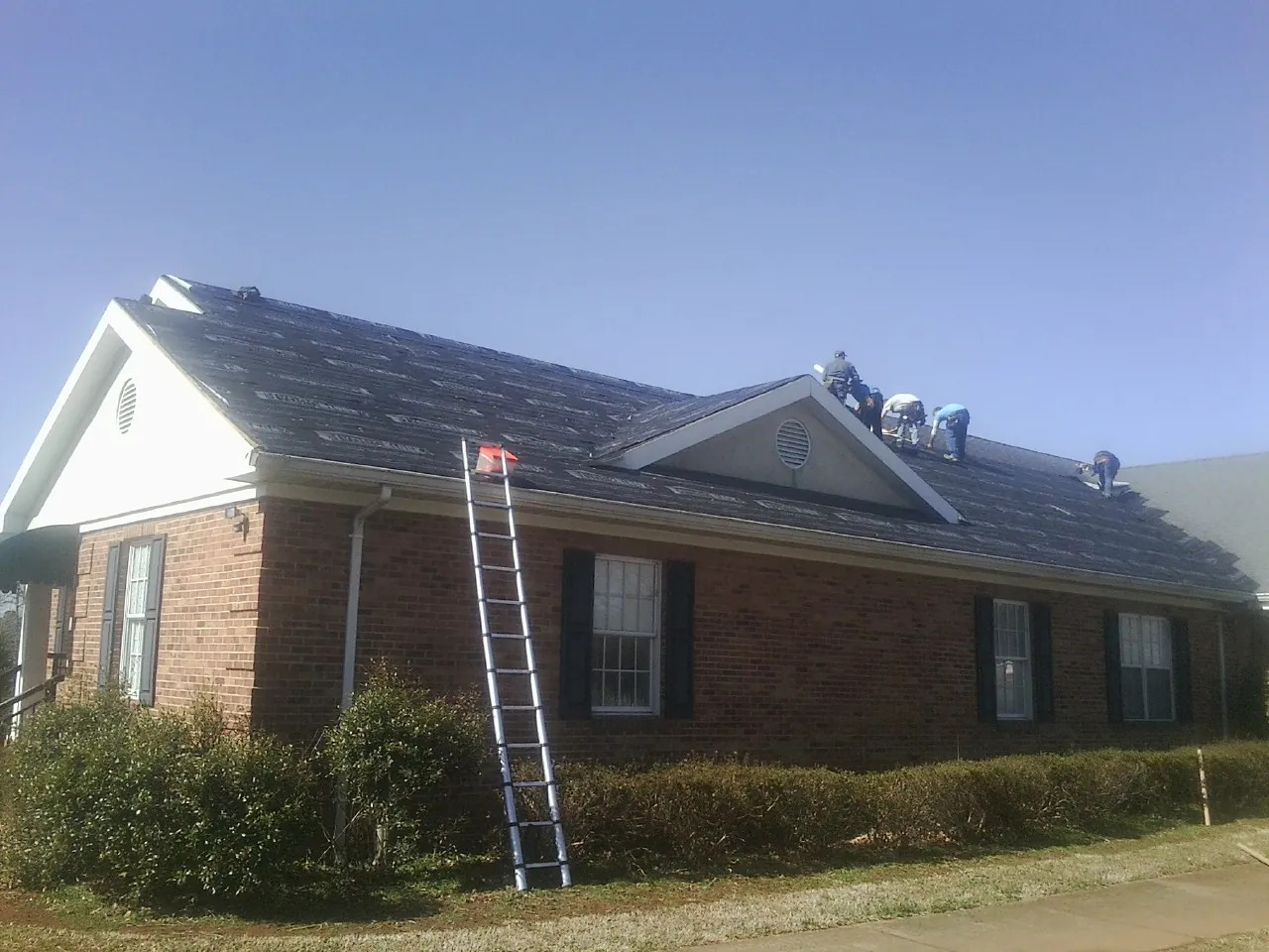 Crew tearing shingles off a brick ranch roof with a ladder set — Emergency Roof Repair work by our crew in Caliente