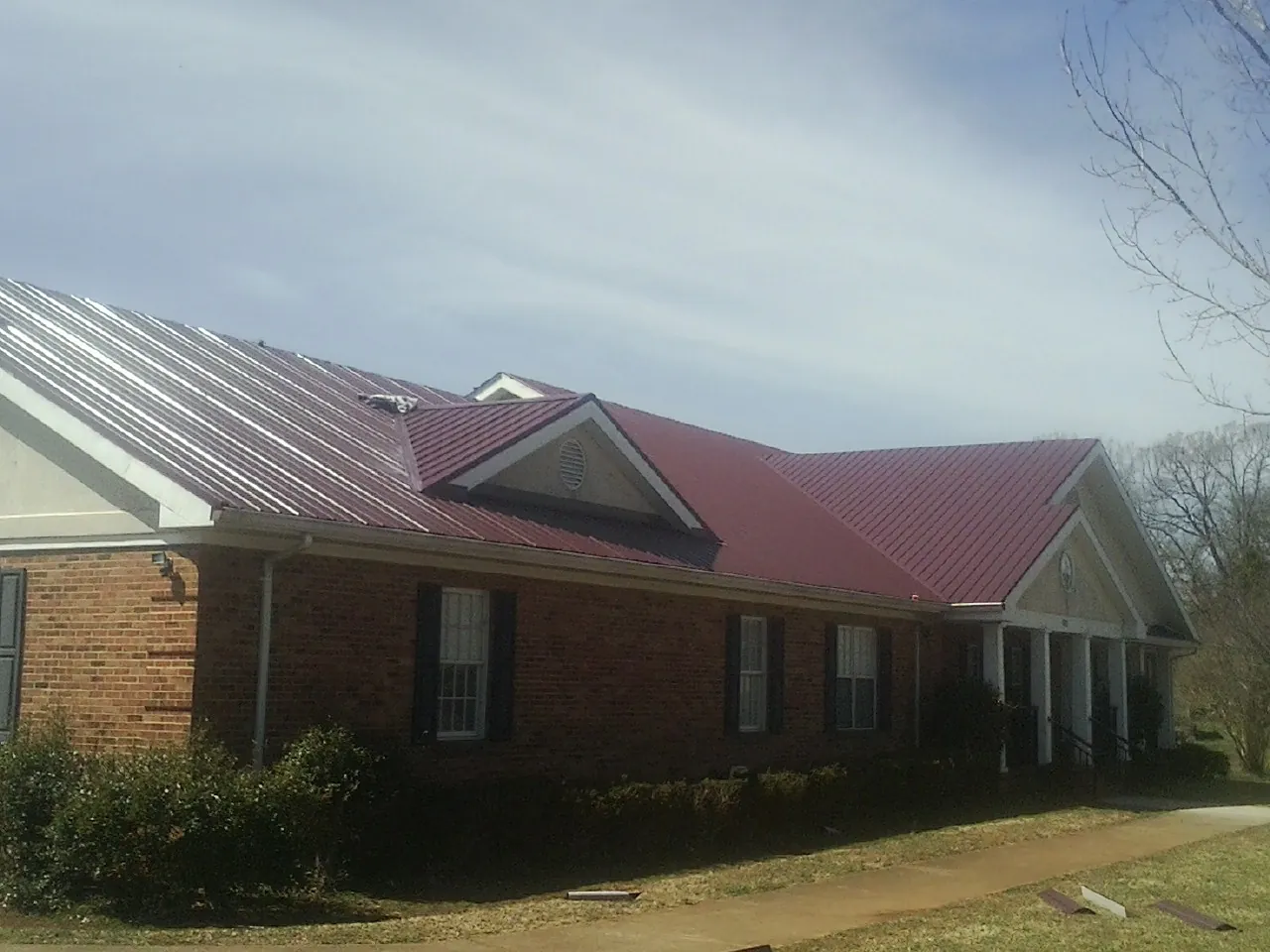 Red metal roof with gabled entries on a long brick building, from a Hail Damage Roof Repair job in Caliente