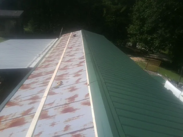 Old rusted panels beside newly installed green metal roofing — Wind Damage Roof Repair by Roofing Brothers in Caliente