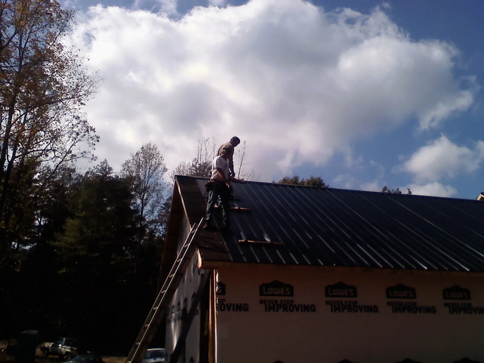 Roofer fastening dark metal panels high against a cloudy sky, from a Roof Inspection job in Caliente